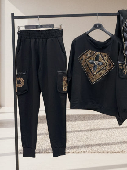 Paparazzi Fashion 3639 Ensemble sport chic sweat et pantalon femme noirs à détails de strass dorés, tenue coordonnée confortable au style urbain chic, à porter avec des baskets pour une allure moderne chic.